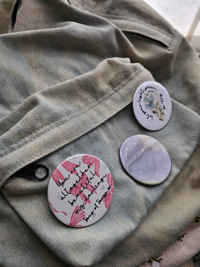 Three circular pins with text and designs on a textured surface