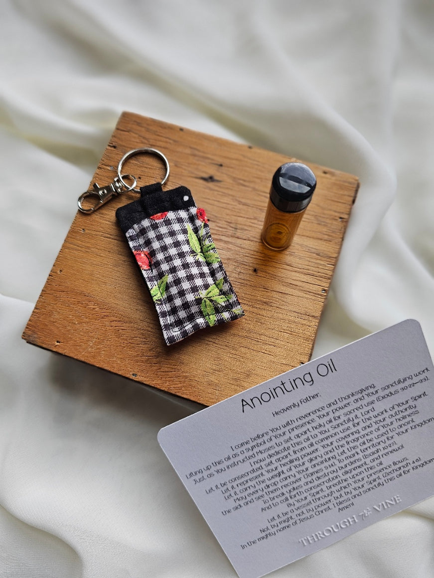 White dots on black, cherries on black and white plaid fabric pouch with a keychain, amber glass bottle, and cardstock card on a wooden block with a white background.