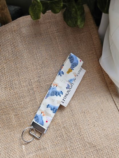 A fabric wristlet keychain with a pigeon patterned print, on a burlap background.