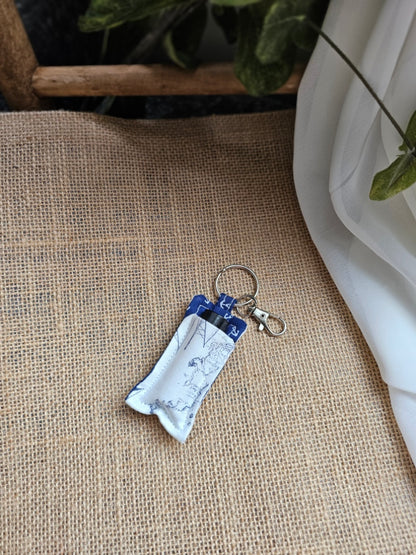 A small fabric keychain oil keeper with map and anchor fabric, resting on a textured beige burlap surface.