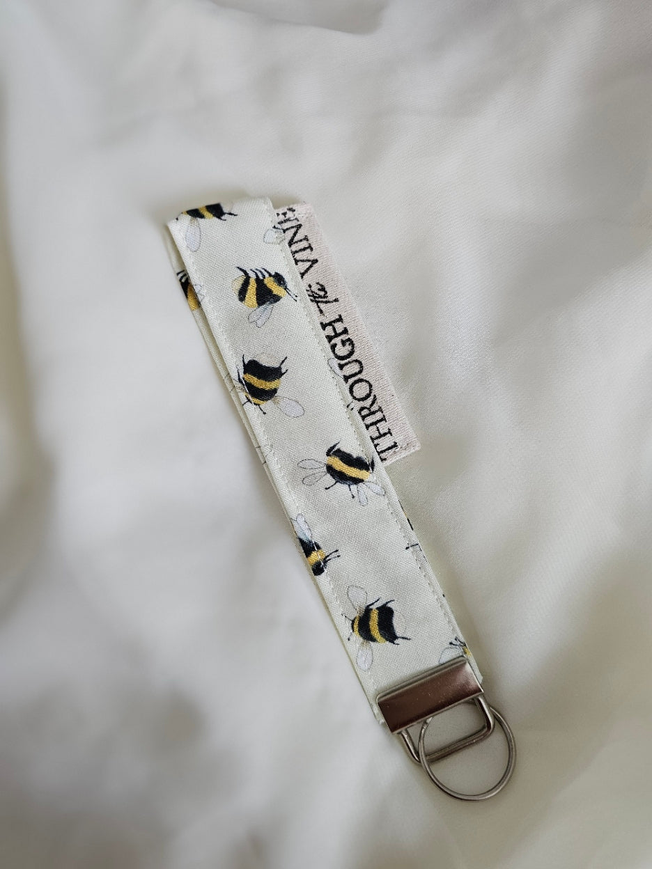 A fabric keychain strap with a white background, with black and yellow bumblebees on fabric.