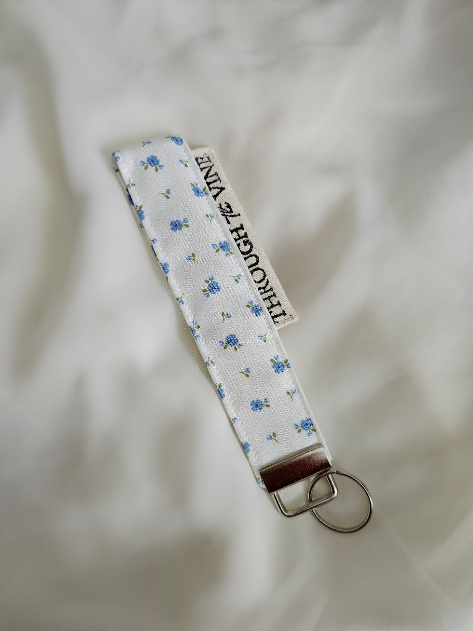 A fabric keychain strap with a white background and a small blue floral pattern.