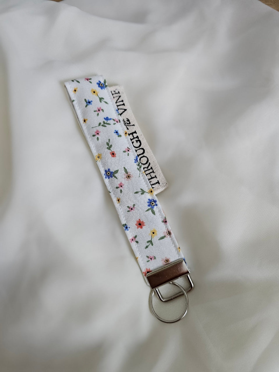 A fabric keychain strap with a white background and a small multicolor floral print.