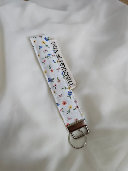 A fabric keychain strap with a white background and a small multicolor floral print.