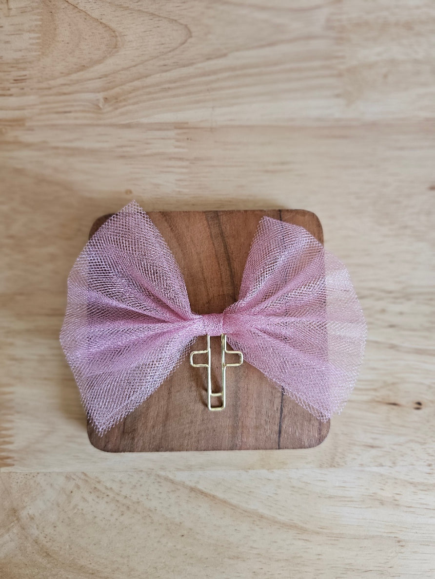 Shimmery pink tulle bow with a gold cross on a wooden box against a wooden background