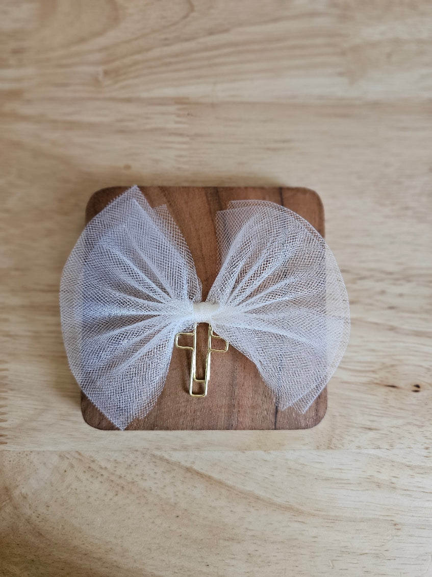 Cream tulle bow with a gold cross on a wooden box against a wooden background