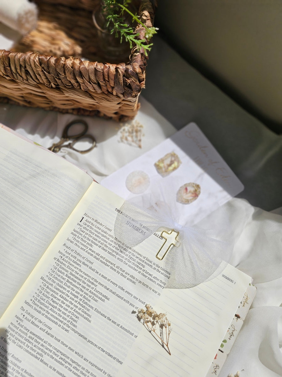 White Tulle bookmark bow including a cross on an open book with a plant beside it and other stationery.