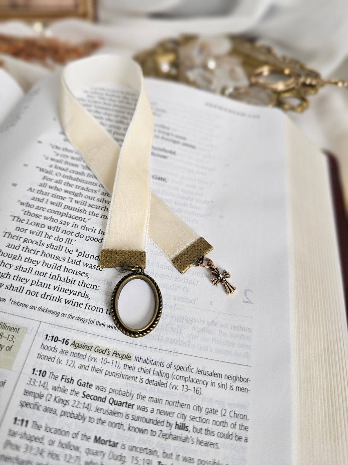Cream velvet ribbon with brass cross and frame charms on each end sitting on top of open Bible. 