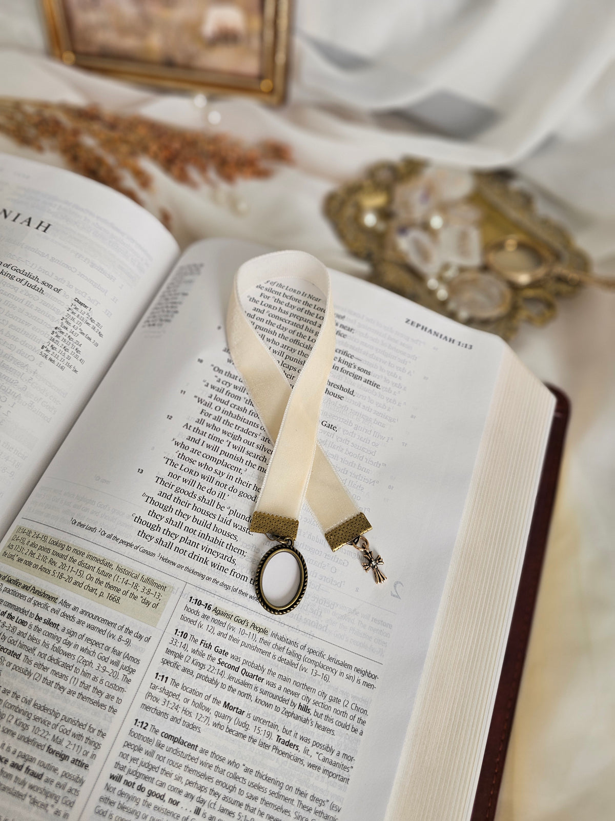 Cream velvet ribbon with brass cross and frame charms on each end sitting on top of open Bible. 