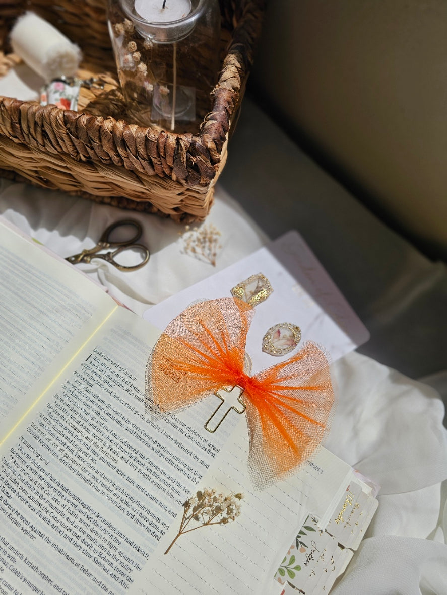 Bright Orange Tulle bookmark bow including a cross on an open book with a plant beside it and other stationery.
