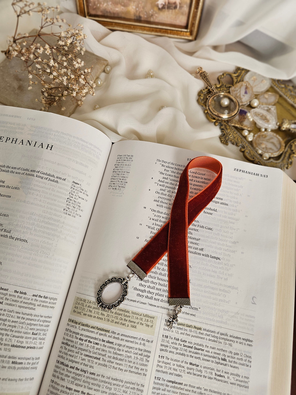 Burnt red-orange velvet ribbon with silver frame and cross charms on each end sitting on an open Bible.