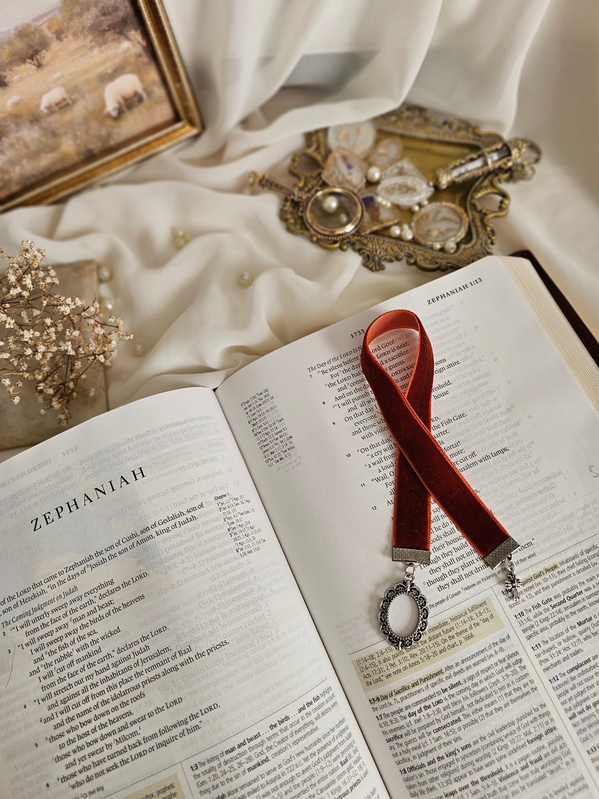 Burnt red-orange velvet ribbon with silver frame and cross charms on each end sitting on an open Bible.