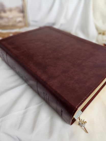Silver crown on gold cross charm sticking out of Bible. 
