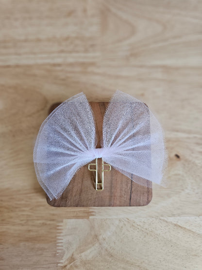 Light pink tulle bow with a gold cross on a wooden box against a wooden background
