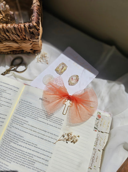 Dull Orange Tulle bookmark bow including a cross on an open book with a plant beside it and other stationery.