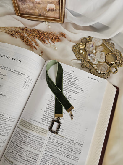Dark green velvet ribbon with brass frame and cross charms on each end sitting on an open Bible.