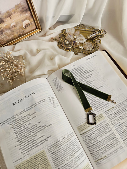 Dark green velvet ribbon with brass frame and cross charms on each end sitting on an open Bible.