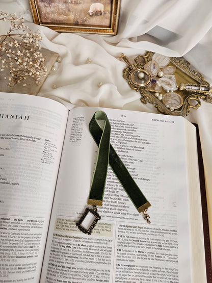 Dark green velvet ribbon with brass frame and cross charms on each end sitting on an open Bible.